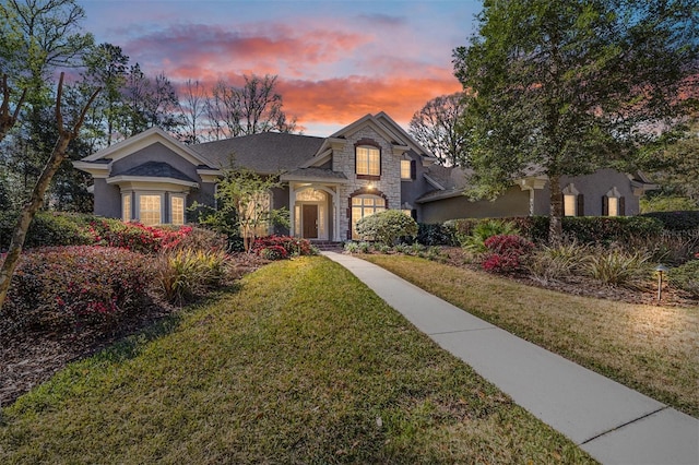 view of front facade featuring stone siding, stucco siding, and a front lawn