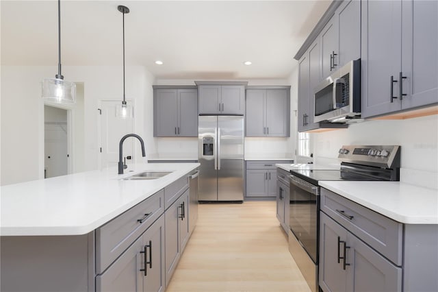 kitchen featuring gray cabinetry, a sink, light countertops, appliances with stainless steel finishes, and light wood finished floors