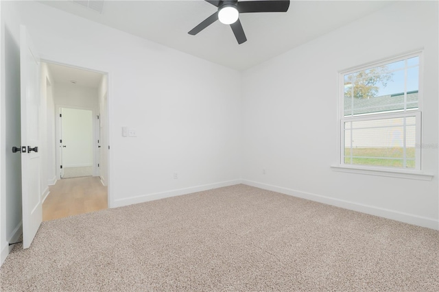 spare room featuring light colored carpet, ceiling fan, visible vents, and baseboards