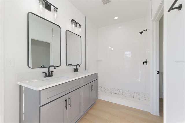 bathroom featuring double vanity, wood finished floors, a sink, and tiled shower