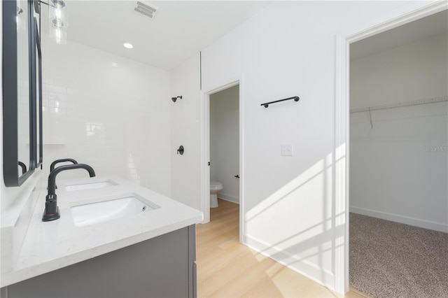 full bath featuring double vanity, visible vents, toilet, wood finished floors, and a sink