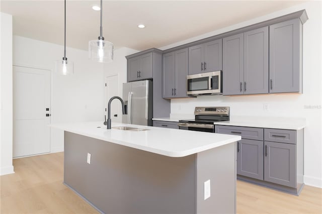 kitchen featuring appliances with stainless steel finishes, a kitchen island with sink, a sink, and gray cabinetry