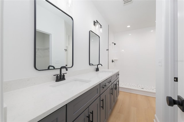 full bathroom with double vanity, tiled shower, a sink, and wood finished floors