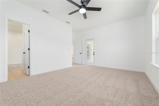 empty room featuring light carpet, a ceiling fan, visible vents, and baseboards