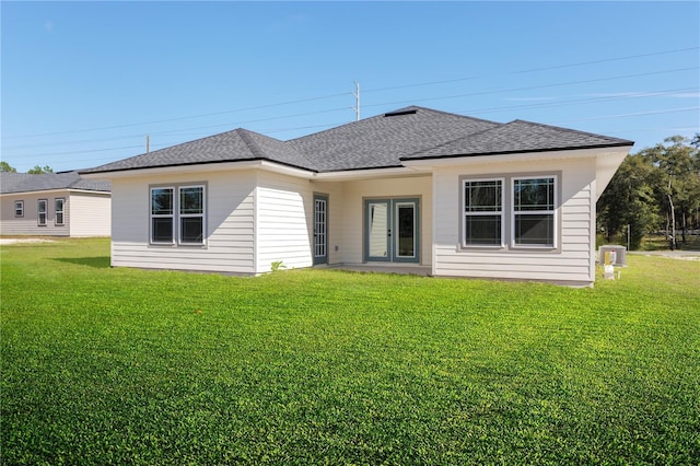 rear view of property featuring roof with shingles, cooling unit, and a lawn