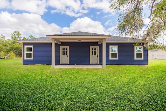 back of property with a shingled roof, a patio area, and a yard