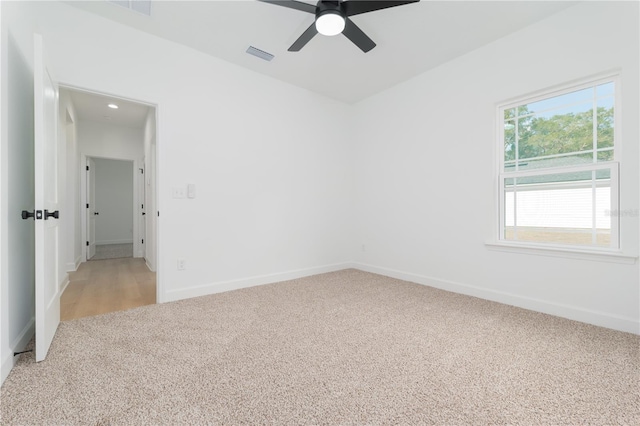 unfurnished room with a ceiling fan, visible vents, light carpet, and baseboards