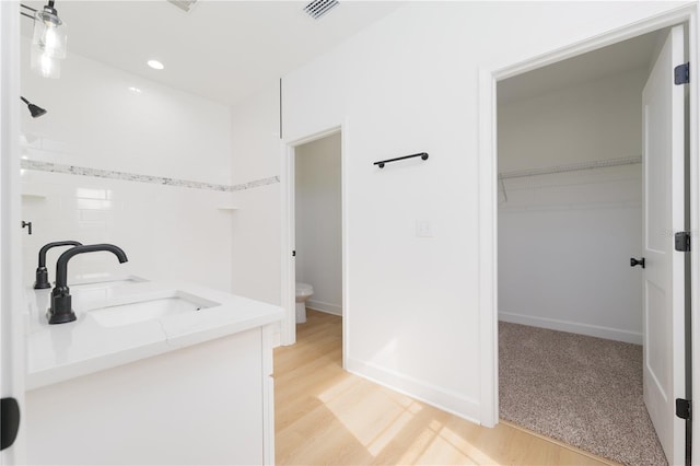 full bath featuring toilet, wood finished floors, a sink, visible vents, and a walk in closet