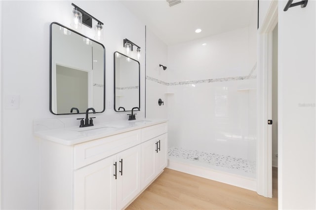 bathroom featuring double vanity, a sink, a tile shower, and wood finished floors