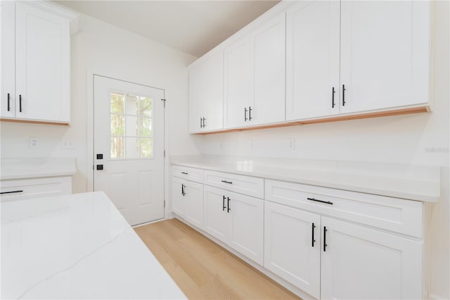 kitchen featuring light wood-type flooring, white cabinetry, and light stone countertops