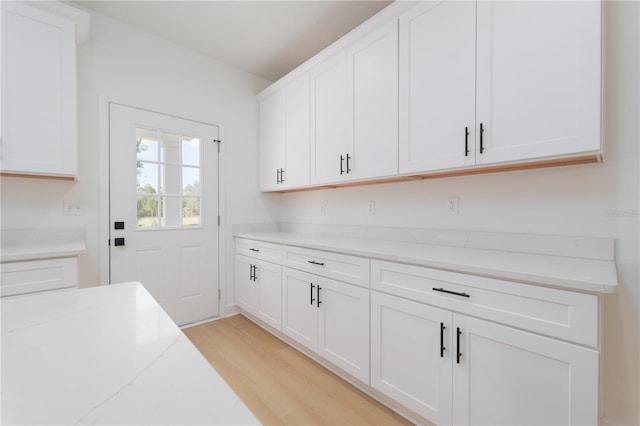 interior space featuring light stone counters, light wood-style flooring, and white cabinets