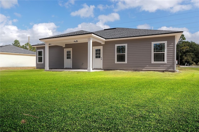 rear view of house with a yard, roof with shingles, and a patio