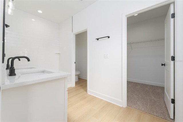 full bathroom with a walk in closet, backsplash, toilet, a sink, and wood finished floors