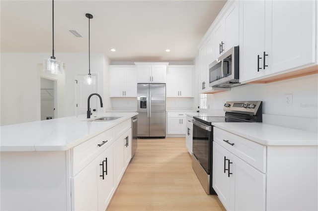 kitchen featuring decorative light fixtures, appliances with stainless steel finishes, white cabinetry, a sink, and light wood-type flooring