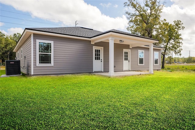 rear view of house featuring a patio area, central AC, a lawn, and roof with shingles