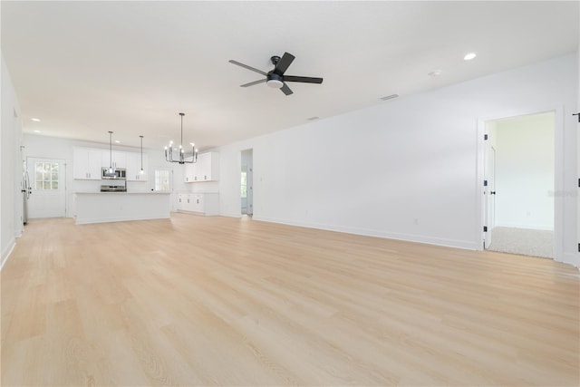 unfurnished living room featuring light wood-type flooring, baseboards, recessed lighting, and ceiling fan with notable chandelier