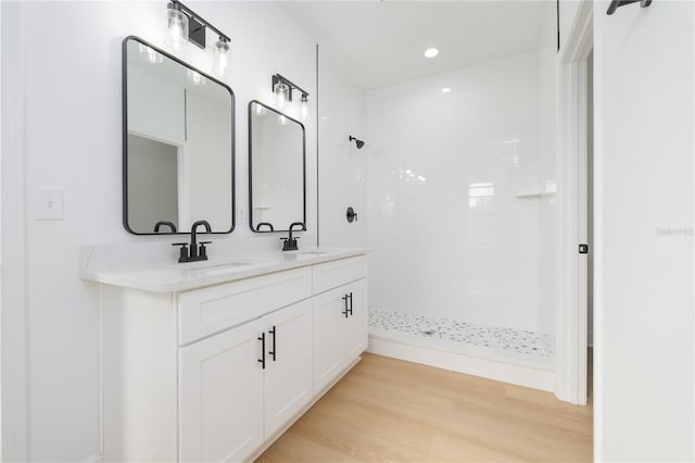 bathroom featuring double vanity, a sink, a tile shower, and wood finished floors