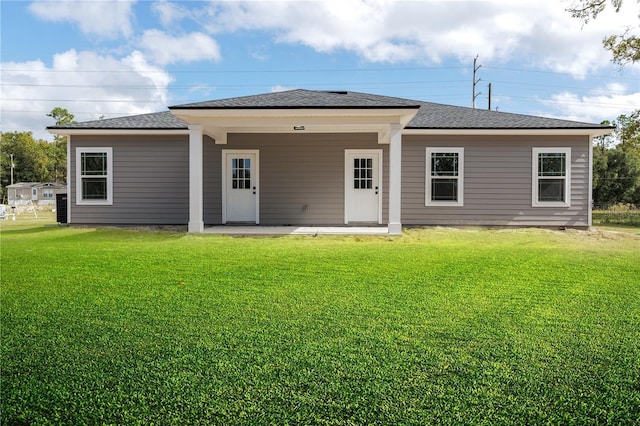 rear view of property with roof with shingles, a lawn, and a patio