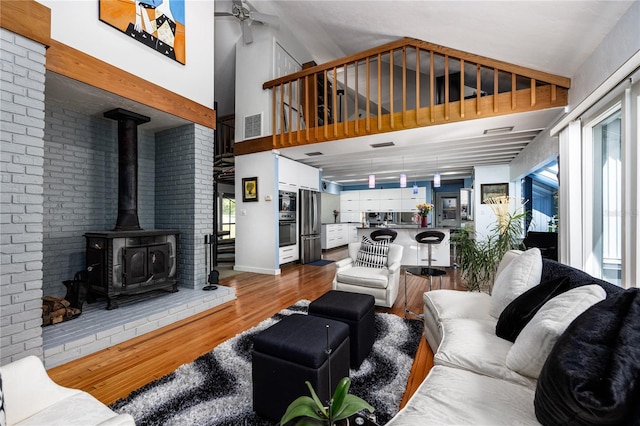 living area with visible vents, ceiling fan, wood finished floors, a wood stove, and high vaulted ceiling