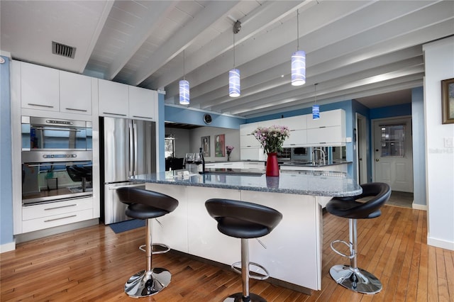 kitchen with appliances with stainless steel finishes, wood-type flooring, visible vents, and white cabinetry