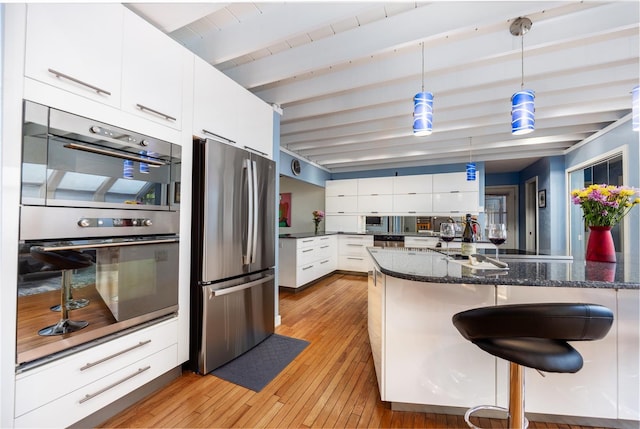 kitchen with stainless steel appliances, beam ceiling, white cabinetry, and a kitchen bar