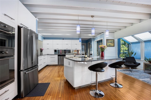 kitchen with modern cabinets, appliances with stainless steel finishes, a breakfast bar area, white cabinetry, and beam ceiling