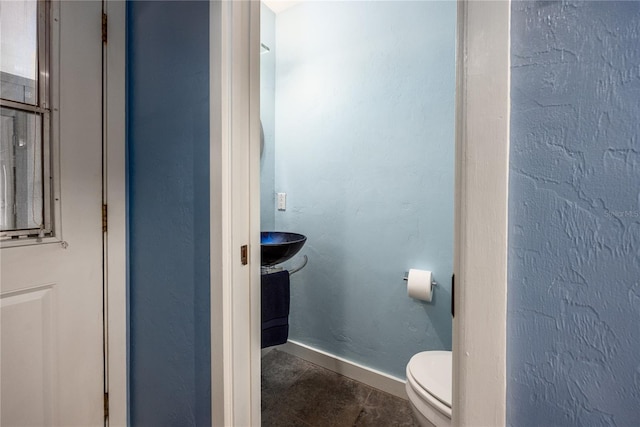 bathroom with toilet, tile patterned flooring, baseboards, and a textured wall