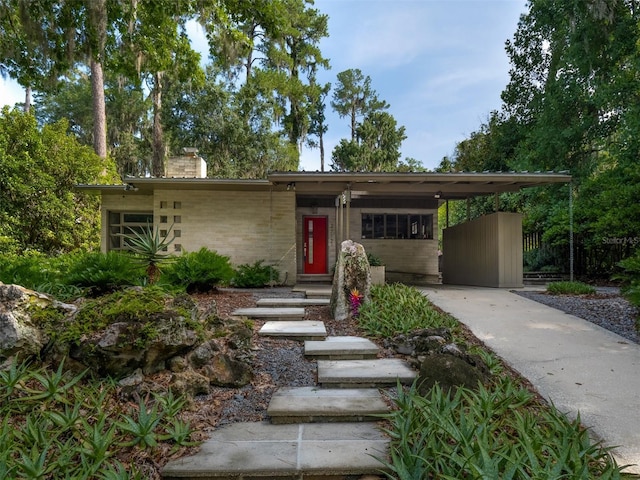 view of front of house featuring driveway, an attached carport, a chimney, and brick siding