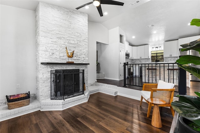 living room with vaulted ceiling, a stone fireplace, wood finished floors, and visible vents