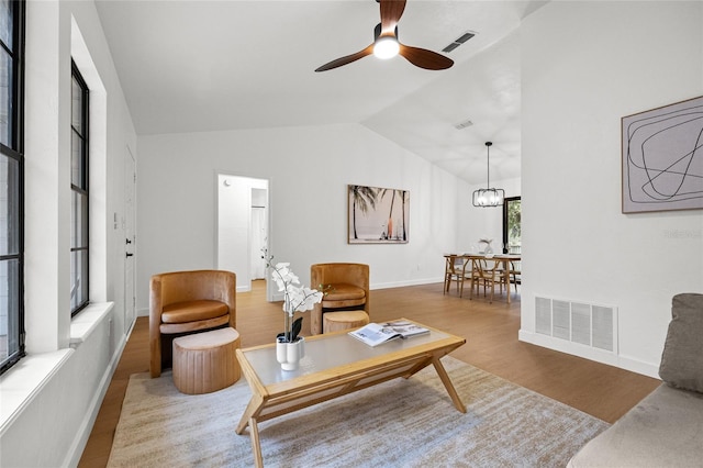 living room featuring visible vents, vaulted ceiling, wood finished floors, and ceiling fan with notable chandelier