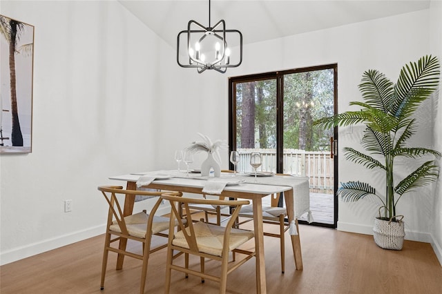 dining space with vaulted ceiling, a notable chandelier, baseboards, and wood finished floors