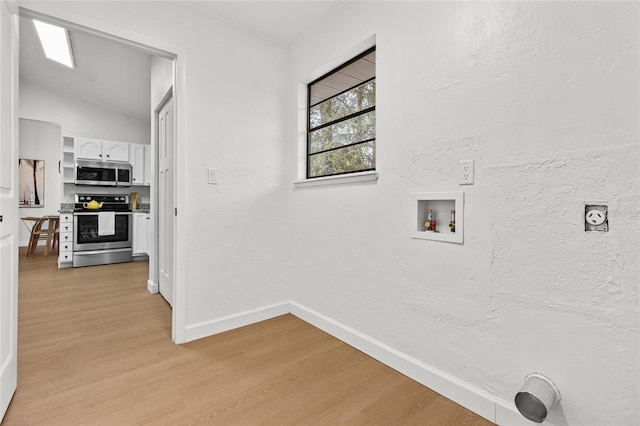 clothes washing area with hookup for a washing machine, a textured wall, light wood-style flooring, and baseboards