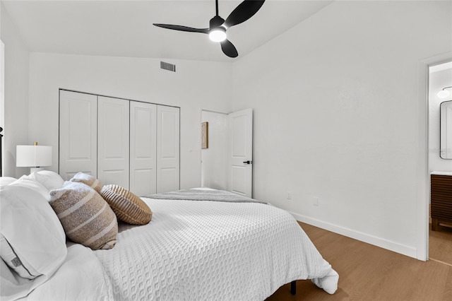 bedroom with a closet, visible vents, vaulted ceiling, wood finished floors, and baseboards