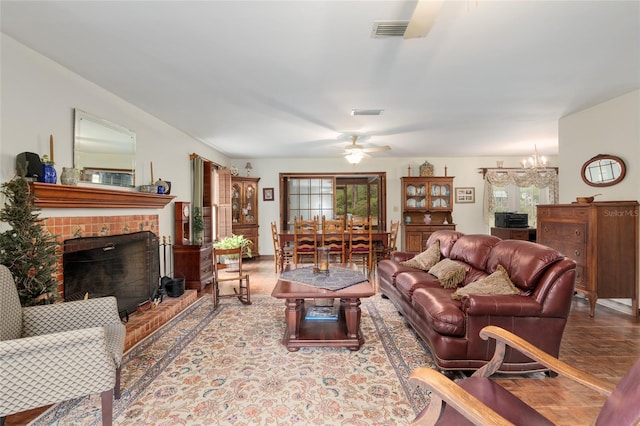 living room featuring a brick fireplace, visible vents, and ceiling fan with notable chandelier