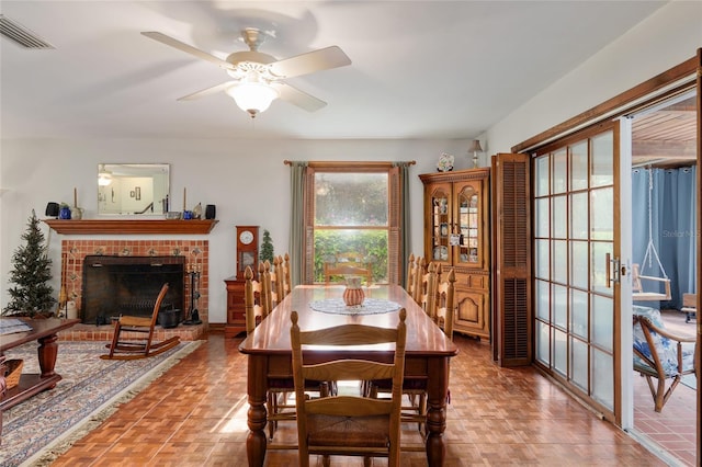 dining space with a brick fireplace, ceiling fan, and visible vents