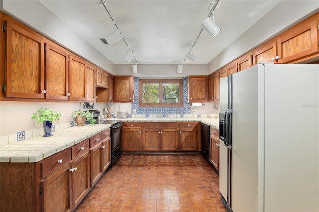 kitchen with tile counters, brown cabinetry, a sink, track lighting, and black appliances