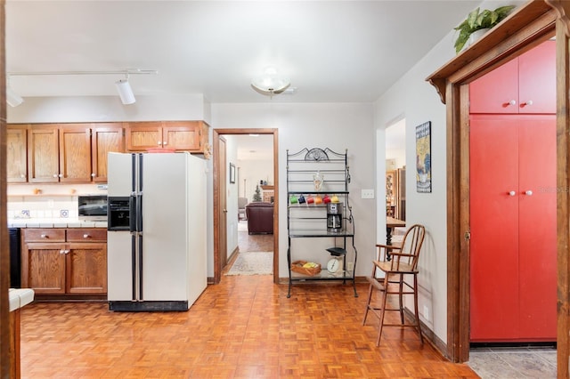 kitchen with white fridge with ice dispenser, stainless steel microwave, and baseboards