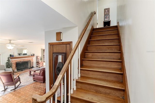 stairs featuring a fireplace, ceiling fan, and wood finished floors