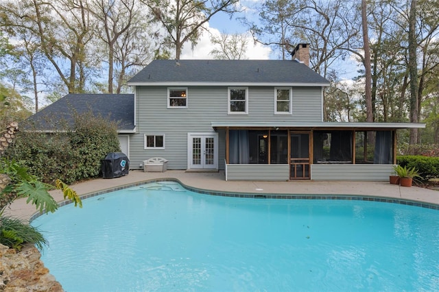 back of property with an outdoor pool, a patio, a sunroom, a chimney, and french doors