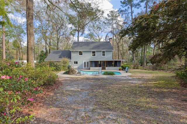 rear view of house featuring a sunroom, a patio area, an outdoor pool, and a chimney