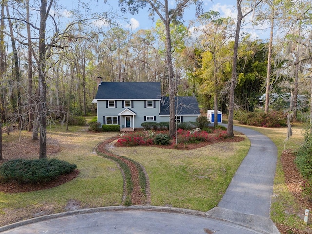 colonial home featuring driveway, a chimney, and a front yard