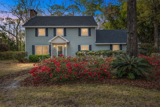 colonial house featuring a shingled roof, a chimney, and a front lawn