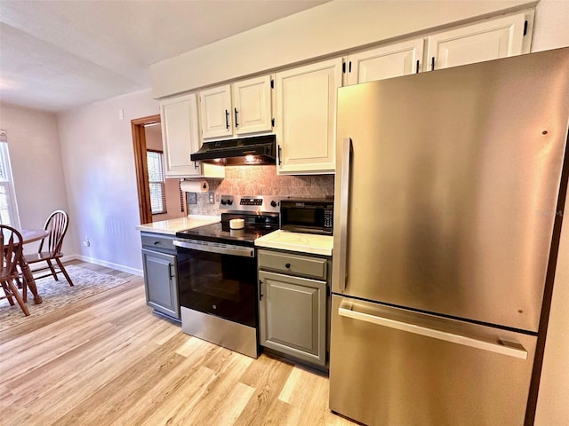 kitchen featuring gray cabinetry, under cabinet range hood, stainless steel appliances, light wood-type flooring, and backsplash