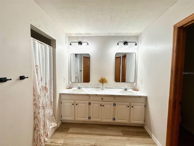 bathroom featuring a sink, double vanity, baseboards, and wood finished floors