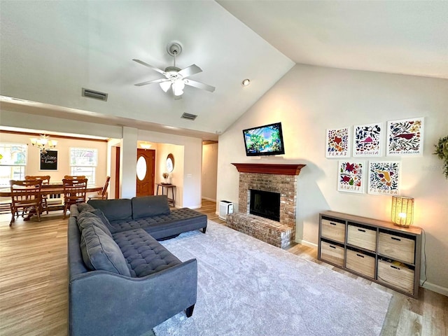 living area with ceiling fan with notable chandelier, a fireplace, wood finished floors, visible vents, and vaulted ceiling