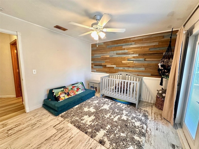 unfurnished bedroom featuring visible vents, an accent wall, ceiling fan, wooden walls, and wood finished floors