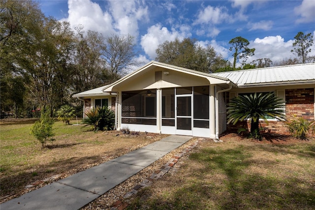 view of front of house featuring a front yard, brick siding, a sunroom, and metal roof