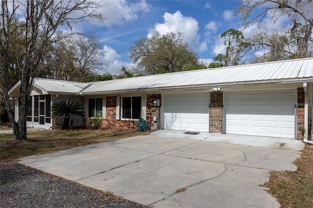 ranch-style home with brick siding, an attached garage, concrete driveway, and metal roof