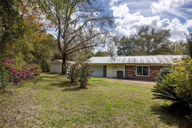 view of front of home with a front yard, central AC, an outdoor structure, brick siding, and metal roof