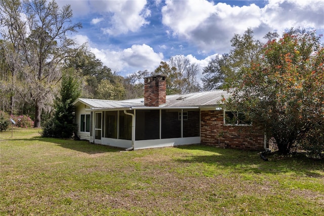 back of property featuring a sunroom, a chimney, a lawn, brick siding, and metal roof